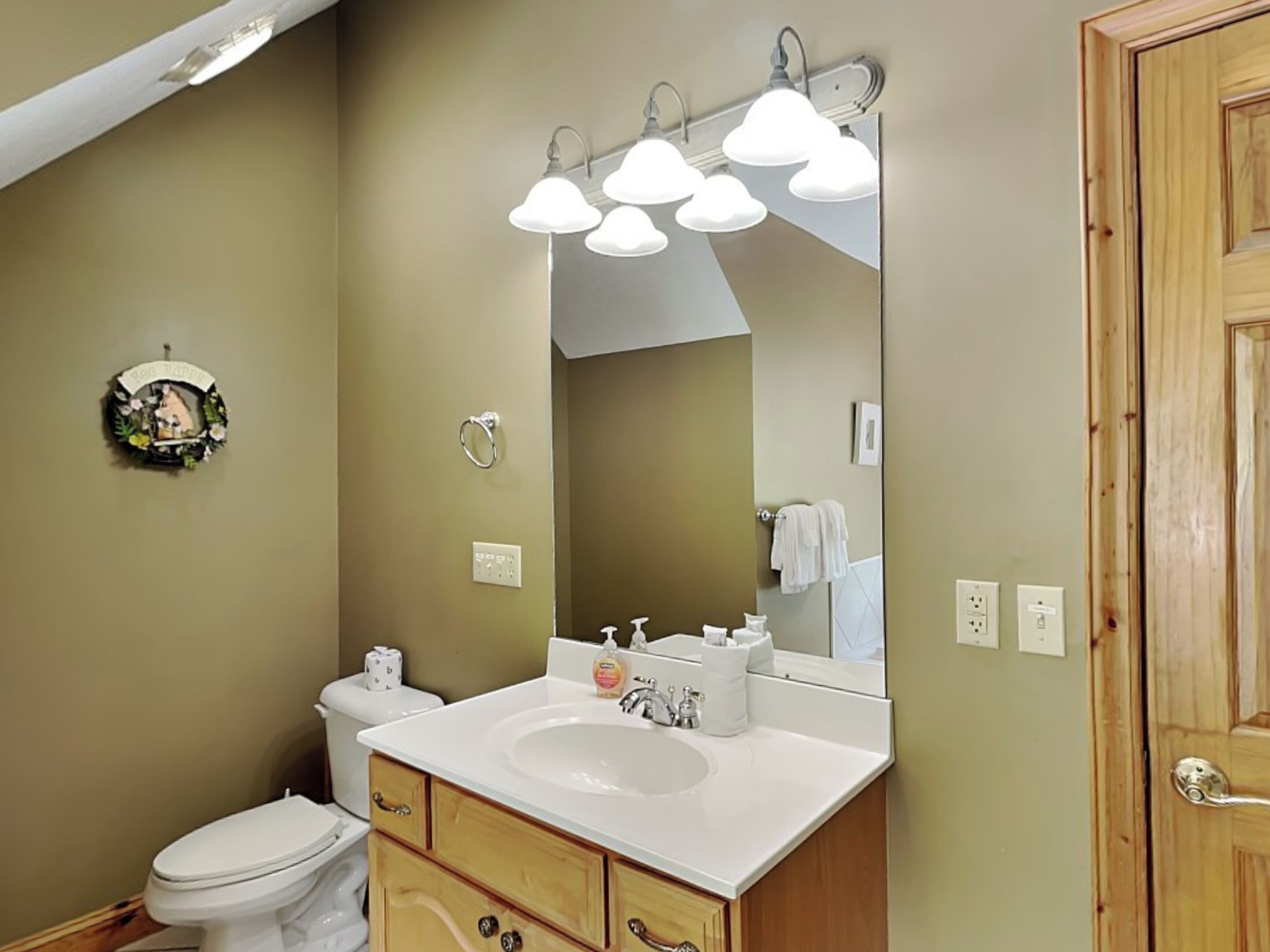 Un baño con lavamanos blanco, mueble de madera y un espejo grande sobre el lavamanos.