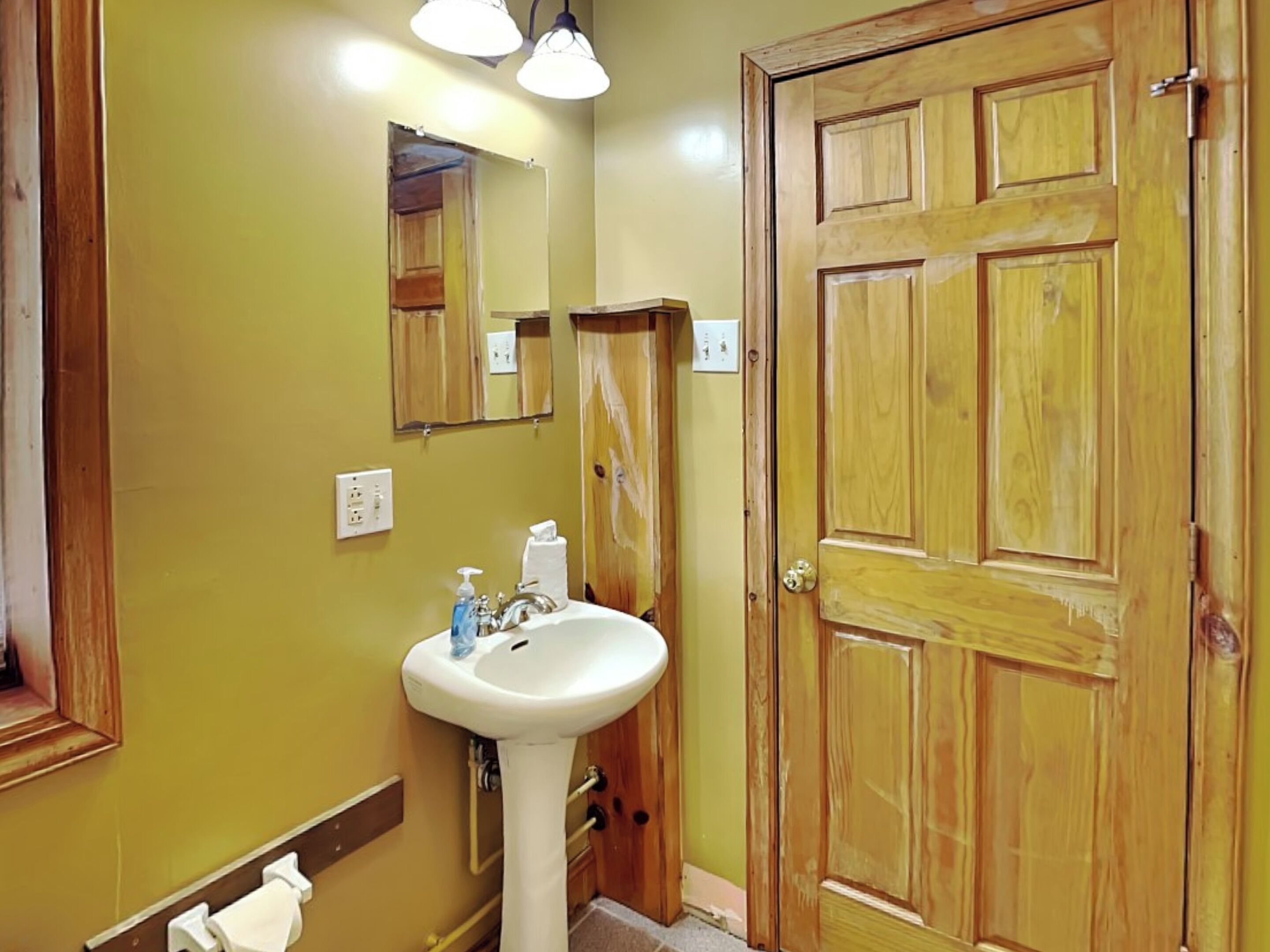 A bathroom with a wooden door, a white sink, and a mirror.
