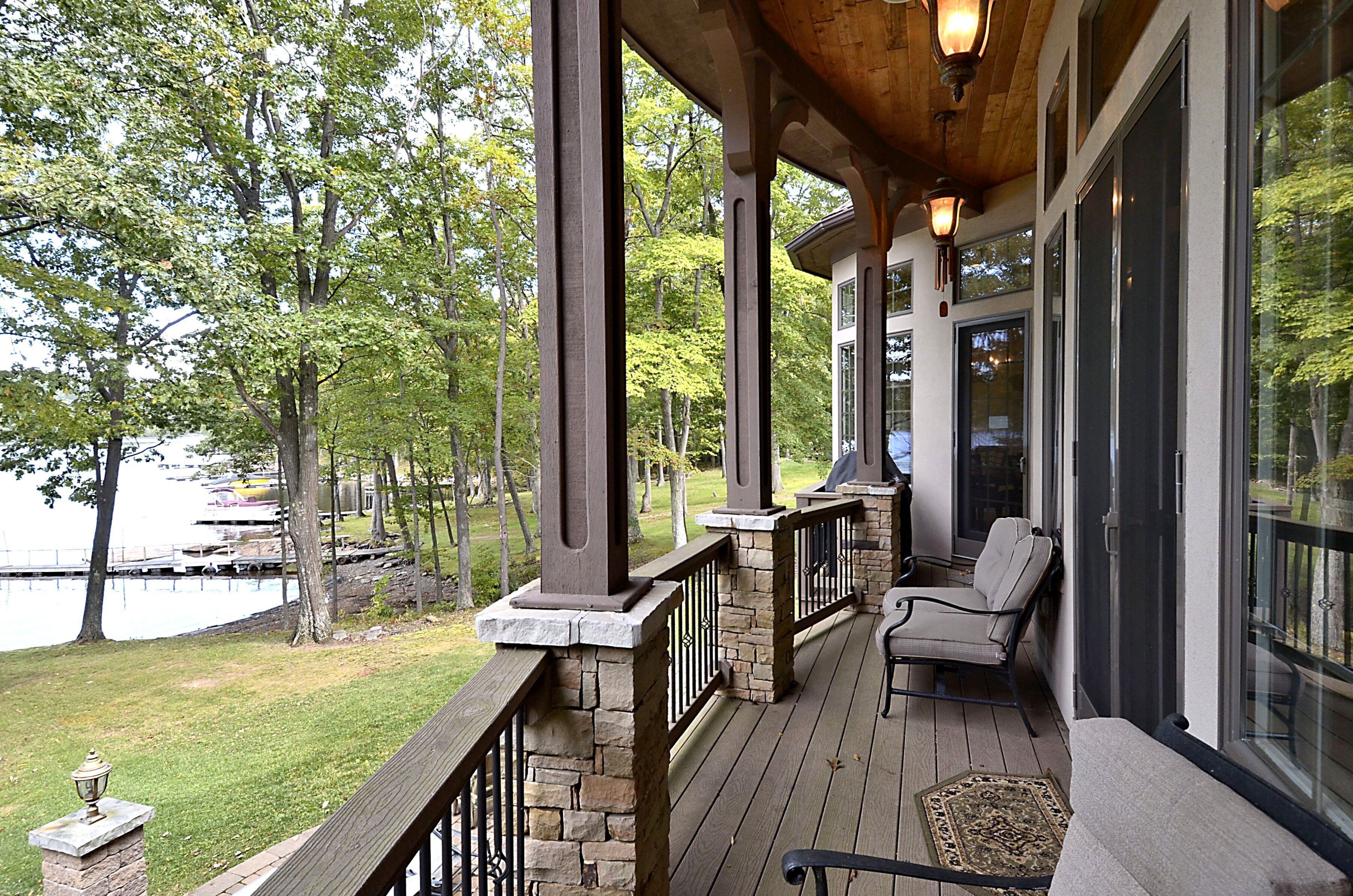 A covered deck with stone pillars, a wooden railing, and a bench.