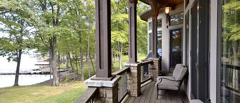 A covered deck with stone pillars, a wooden railing, and a bench.