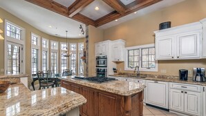 A spacious kitchen with a large island, white cabinetry, and a stone fireplace. - Champagne Taste by Taylor Made Deep Creek (Oakland)