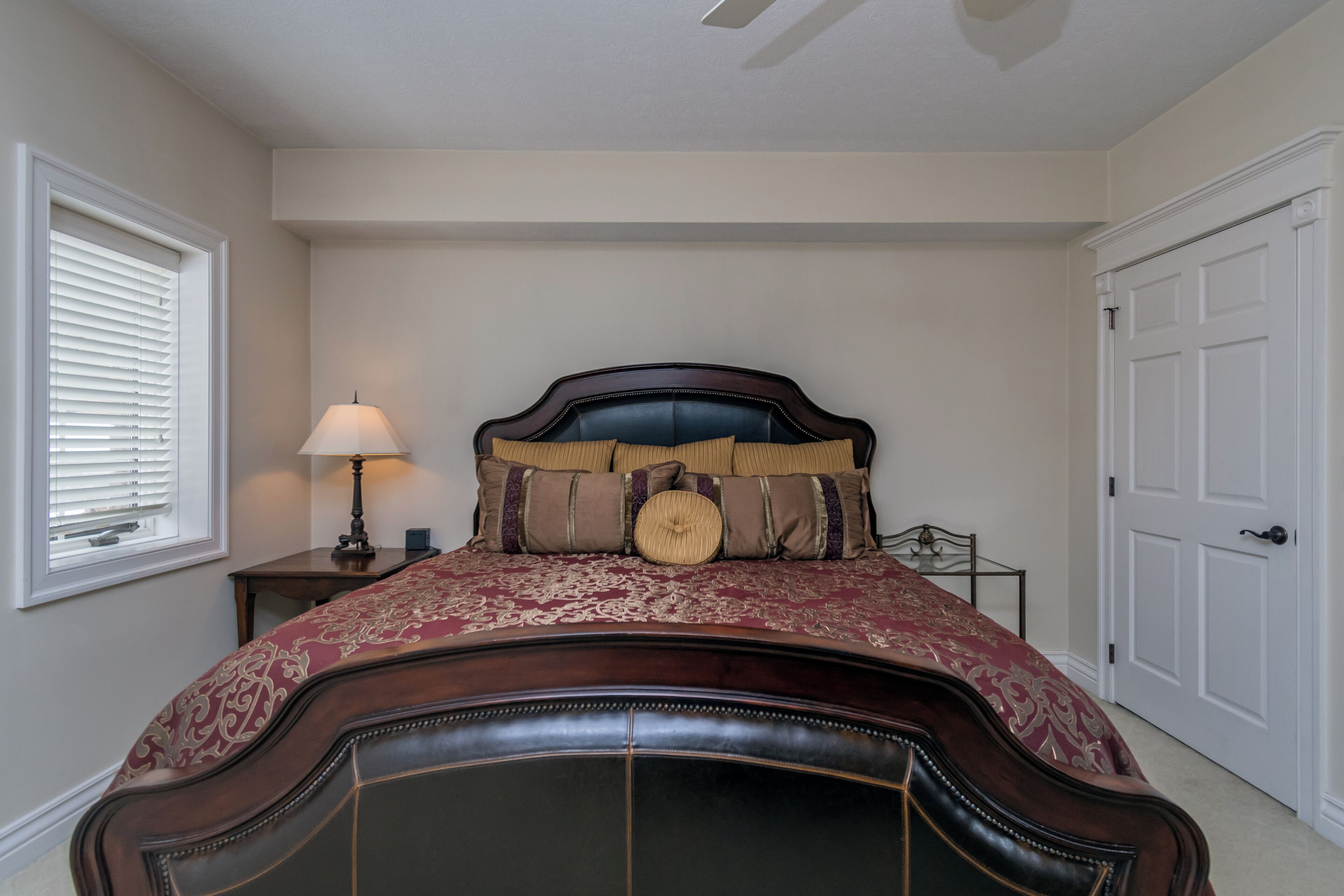 A bedroom with a large bed, a bedside table with a lamp, and a door.