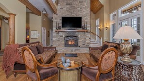 A spacious living room with a stone fireplace, comfortable seating, and a television. - Champagne Taste by Taylor Made Deep Creek (Oakland)