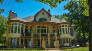 A large, two-story house with a wrap-around porch, stone exterior, and multiple windows. - Champagne Taste by Taylor Made Deep Creek (Oakland)