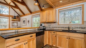 Una cocina con armarios de madera, lavavajillas, encimera de granito y ventana con vista a árboles.