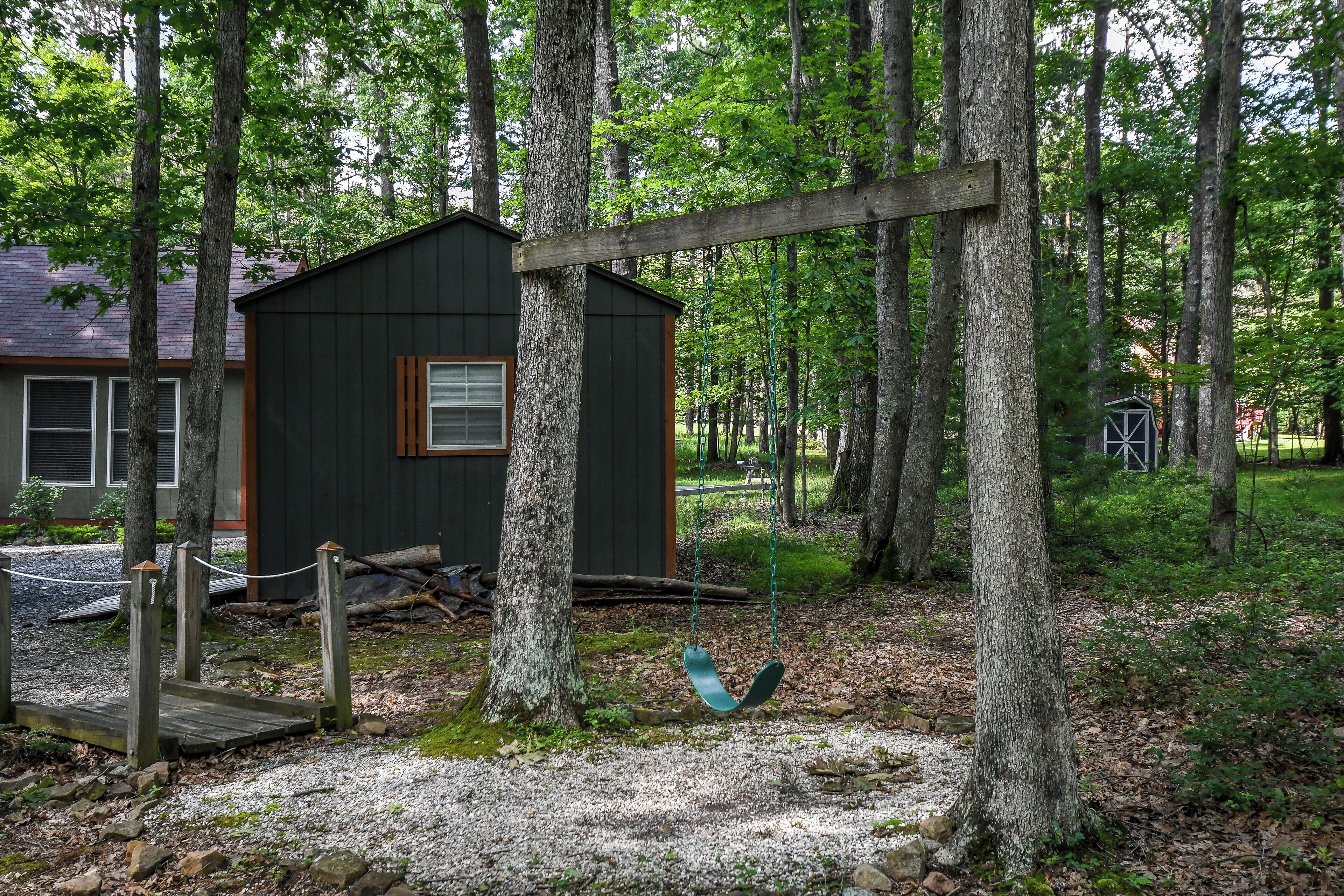 A wooden swing set in a wooded area with a small cabin.