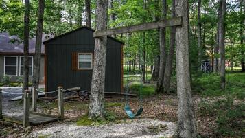 A wooden swing set in a wooded area with a small cabin.
