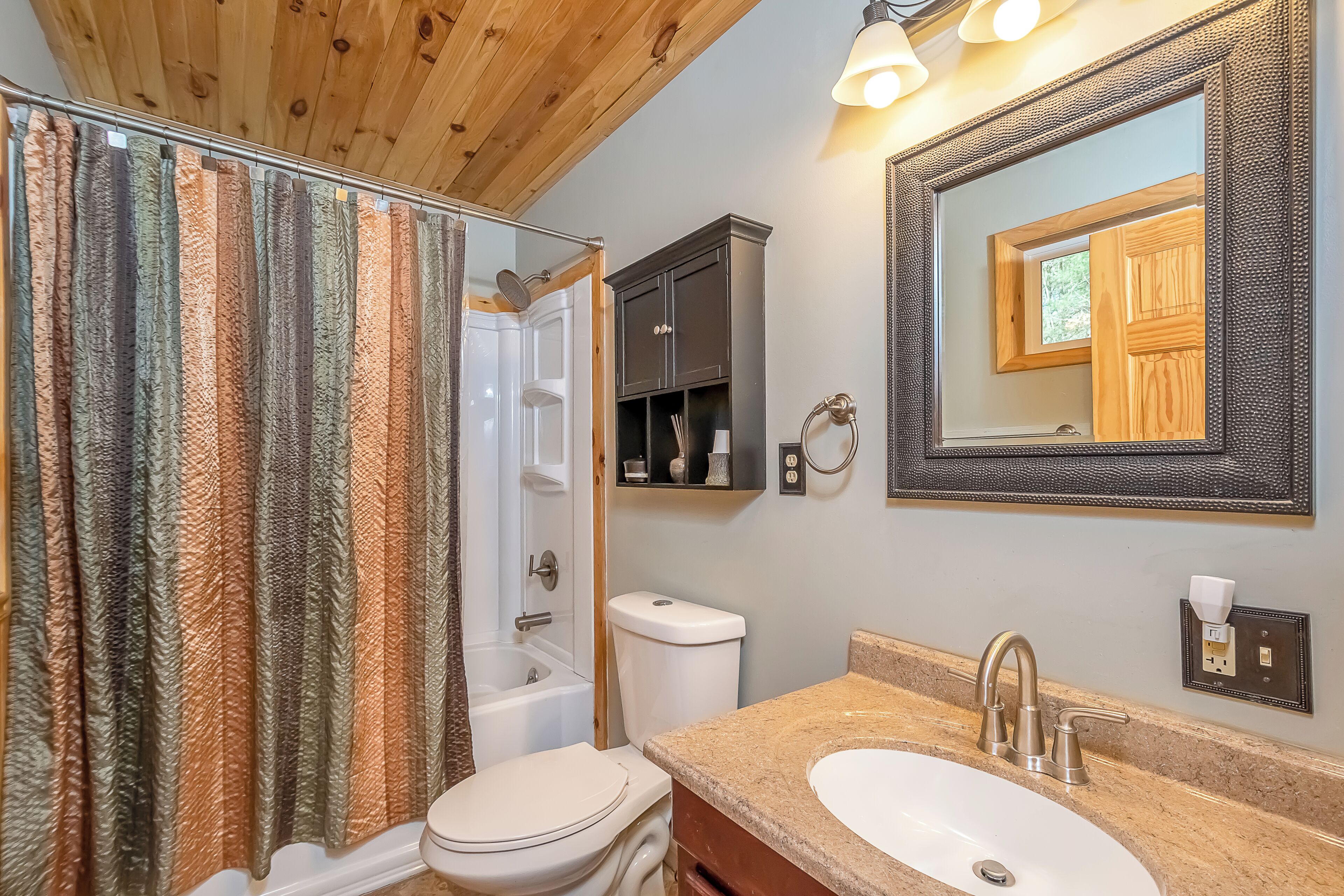 A bathroom with a shower curtain, toilet, bathtub, vanity with a sink, and a mirror.