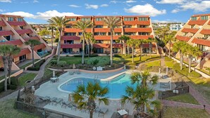 A hotel with a pool, outdoor seating, and palm trees. - Aegean #332 - Gulf-Front Views, Relaxing Amenities (Destin)