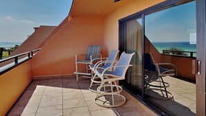 A balcony with two wicker chairs and a table, a glass door, and a view of the ocean. - Aegean #332 - Gulf-Front Views, Relaxing Amenities (Destin)