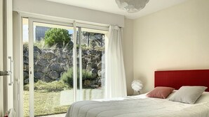 A bedroom with a bed, a red headboard, and a view of a rocky outdoor area through a sliding glass door. - VILLA LA COTINIERE (Saint-Pierre-d'Oléron)