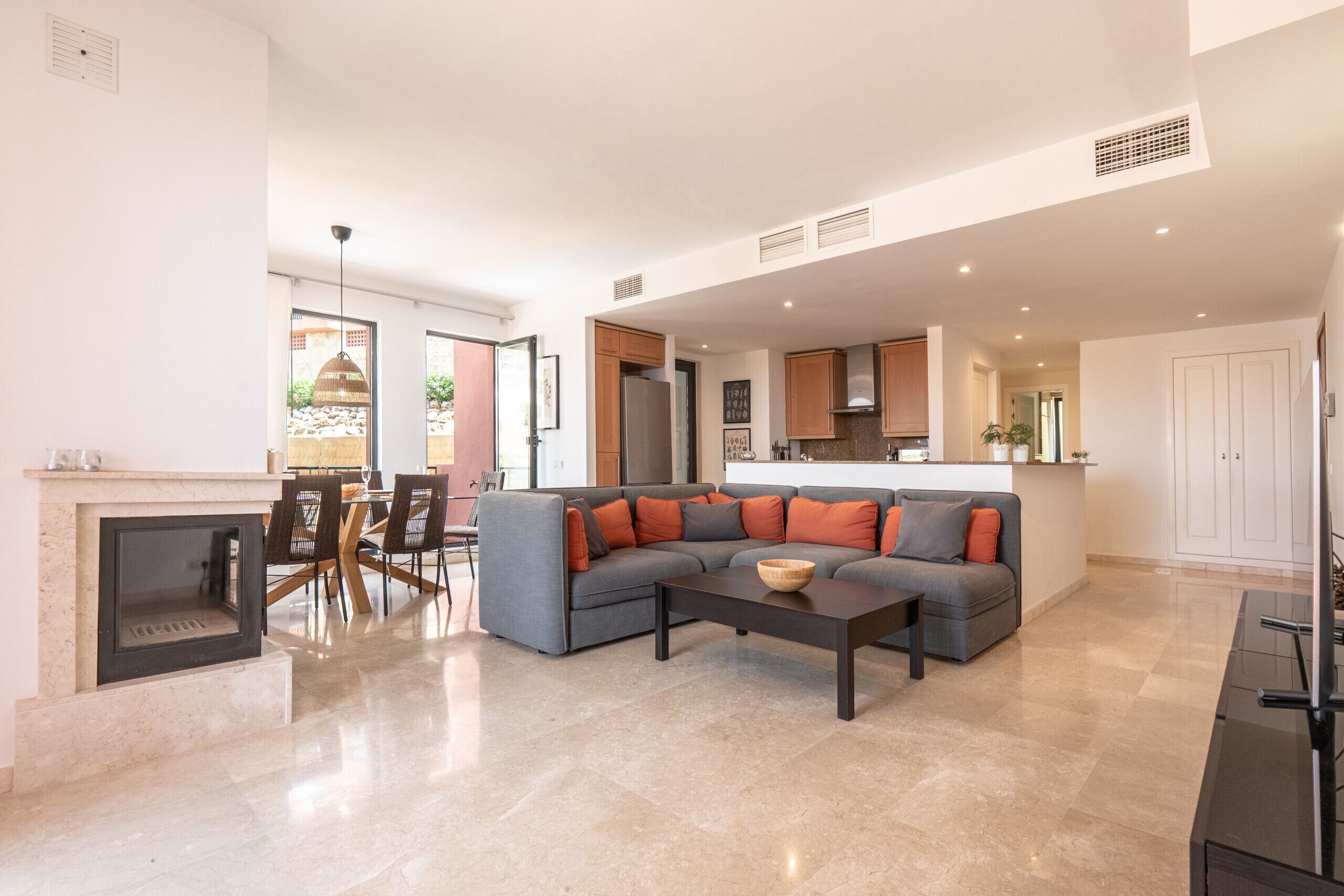 Una sala de estar moderna con chimenea, un sofá seccional gris y un comedor con mesa y sillas.