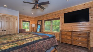 A bedroom with a large bed, wooden walls, a ceiling fan, a TV, and a dresser. - Cj's Mountain Lodge by Taylor Made Deep Creek (McHenry)
