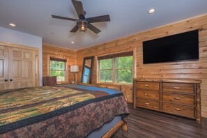 Une chambre avec un grand lit, des murs en bois, un ventilateur de plafond, une télévision et une commode.
