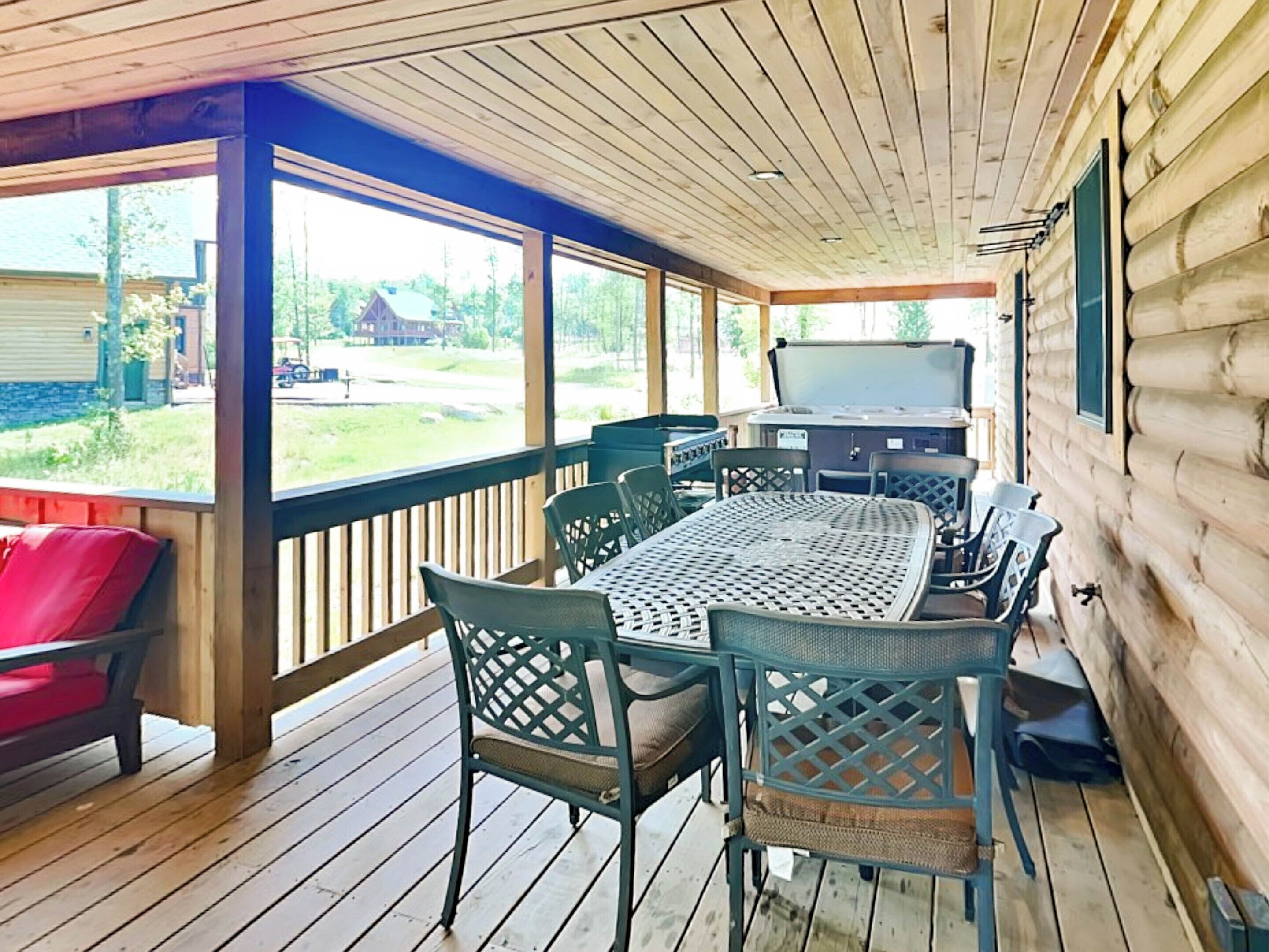 A covered outdoor area with a wooden deck, a table with chairs, and a grill.