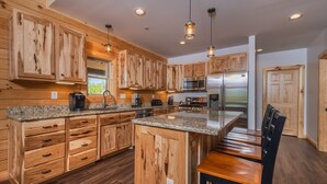 A modern kitchen with wooden cabinetry, granite countertops, and stainless steel appliances. - Cj's Mountain Lodge by Taylor Made Deep Creek (McHenry)