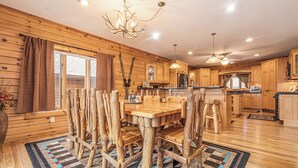 A rustic cabin interior with a wooden dining table surrounded by chairs, a kitchen area, and a chandelier. - Colorado Dreamin' by Taylor Made Deep Creek (McHenry)