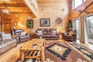 Ein gemütliches Blockhaus-Interieur mit Holzwänden, Ledersofas, einem Holztisch und einem Teppich mit geometrischem Muster.