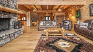 A spacious living area with a stone fireplace, wooden flooring, a large sofa, a leather armchair, and a patterned rug. - Colorado Dreamin' by Taylor Made Deep Creek (McHenry)
