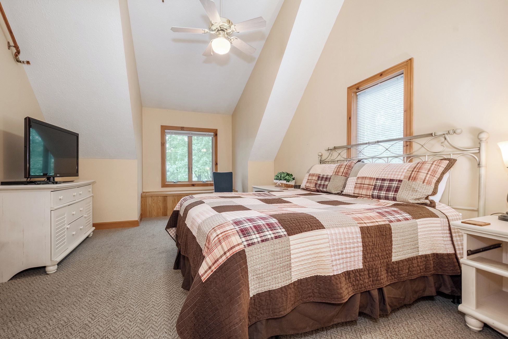 A bedroom with a bed, a television, a ceiling fan, and a window.