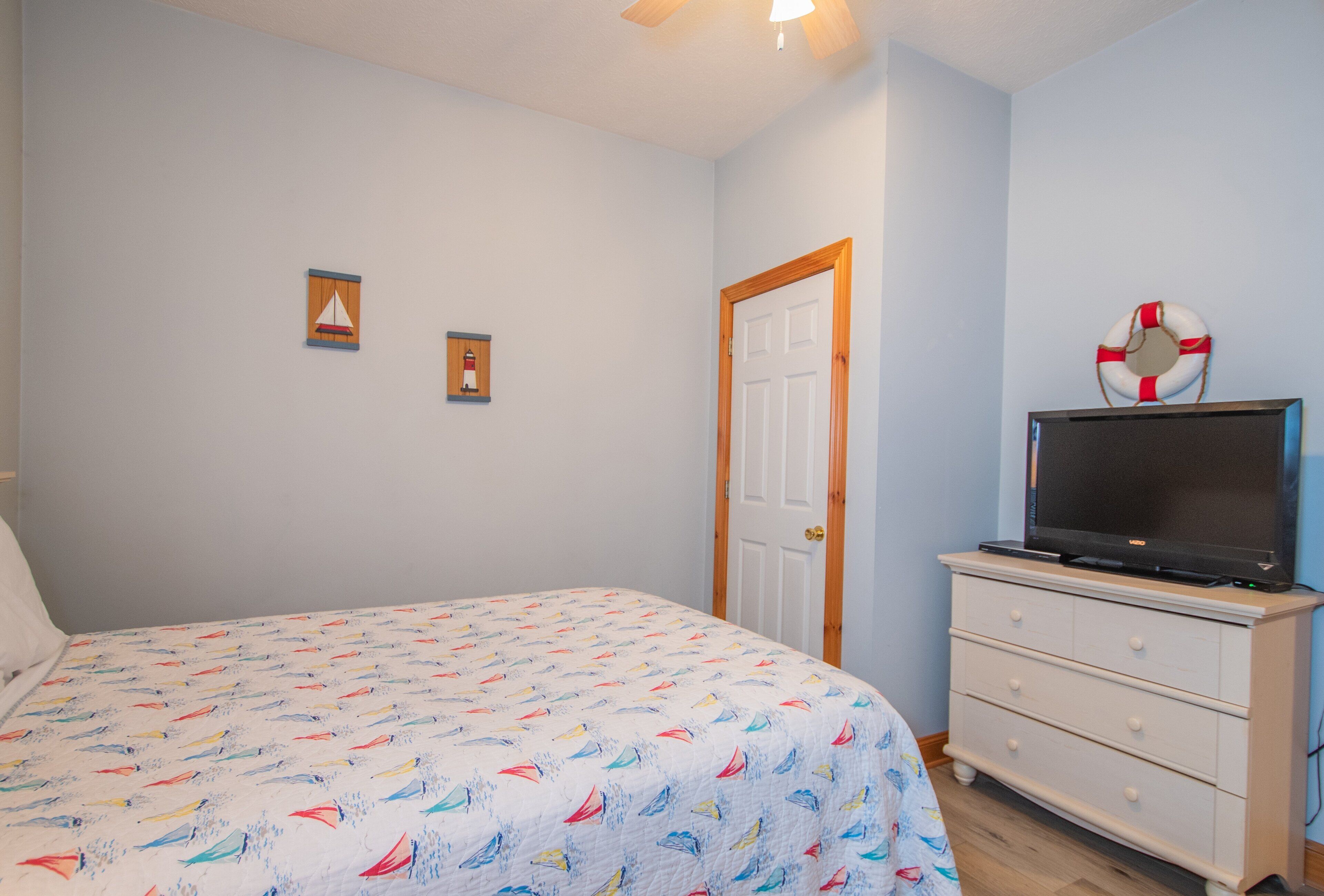 A bedroom with a bed, a dresser, a television on top, and a door with a wooden frame.