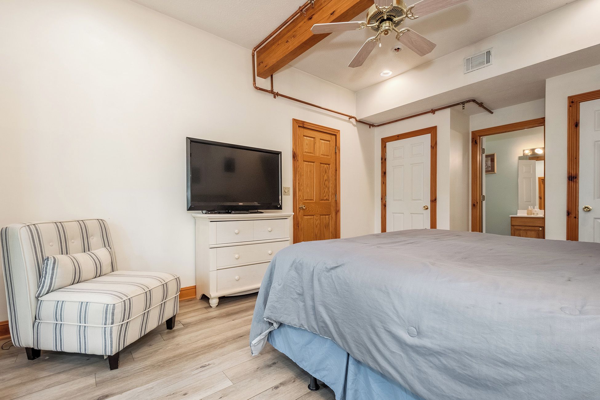 A bedroom with a bed, a television on a dresser, a chair, and wooden doors.