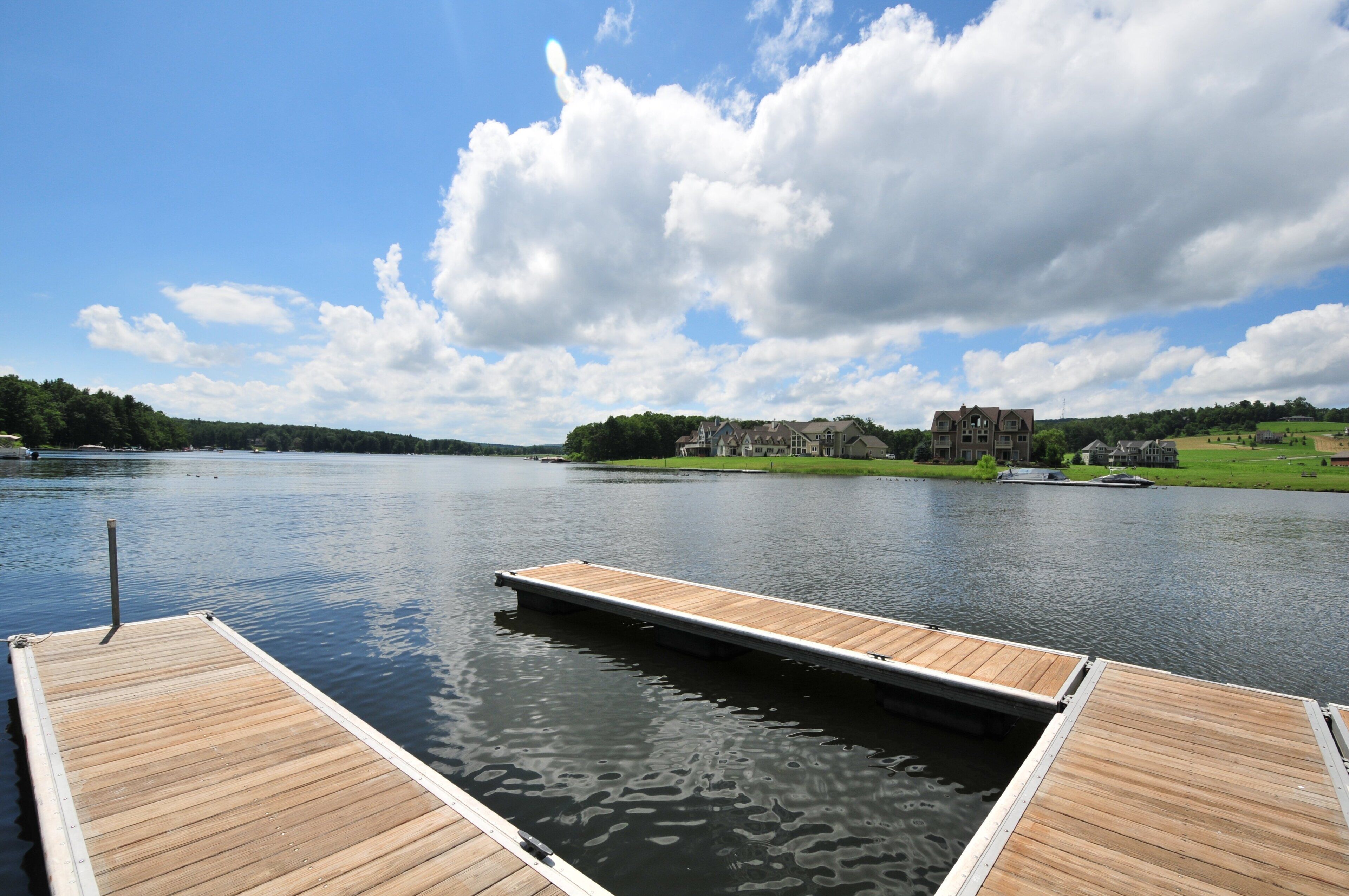 A wooden dock extending into a calm lake with a large house in the background.