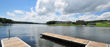 A wooden dock extending into a calm lake with a large house in the background.