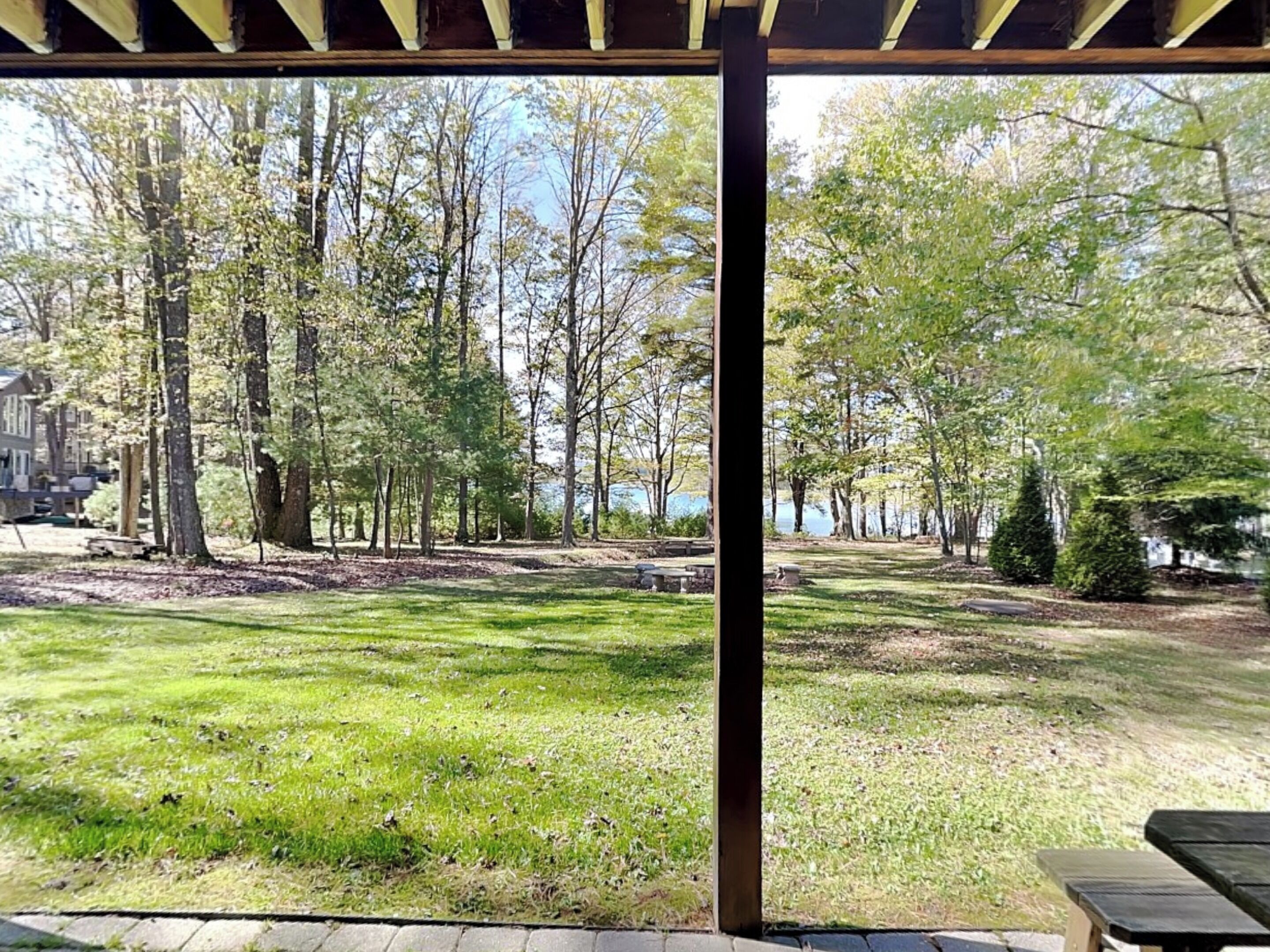 A covered outdoor area with a grassy lawn, trees, and a view of a body of water.