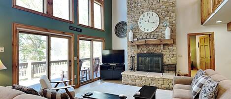 A spacious living room with a stone fireplace, large windows, and a cozy seating area.