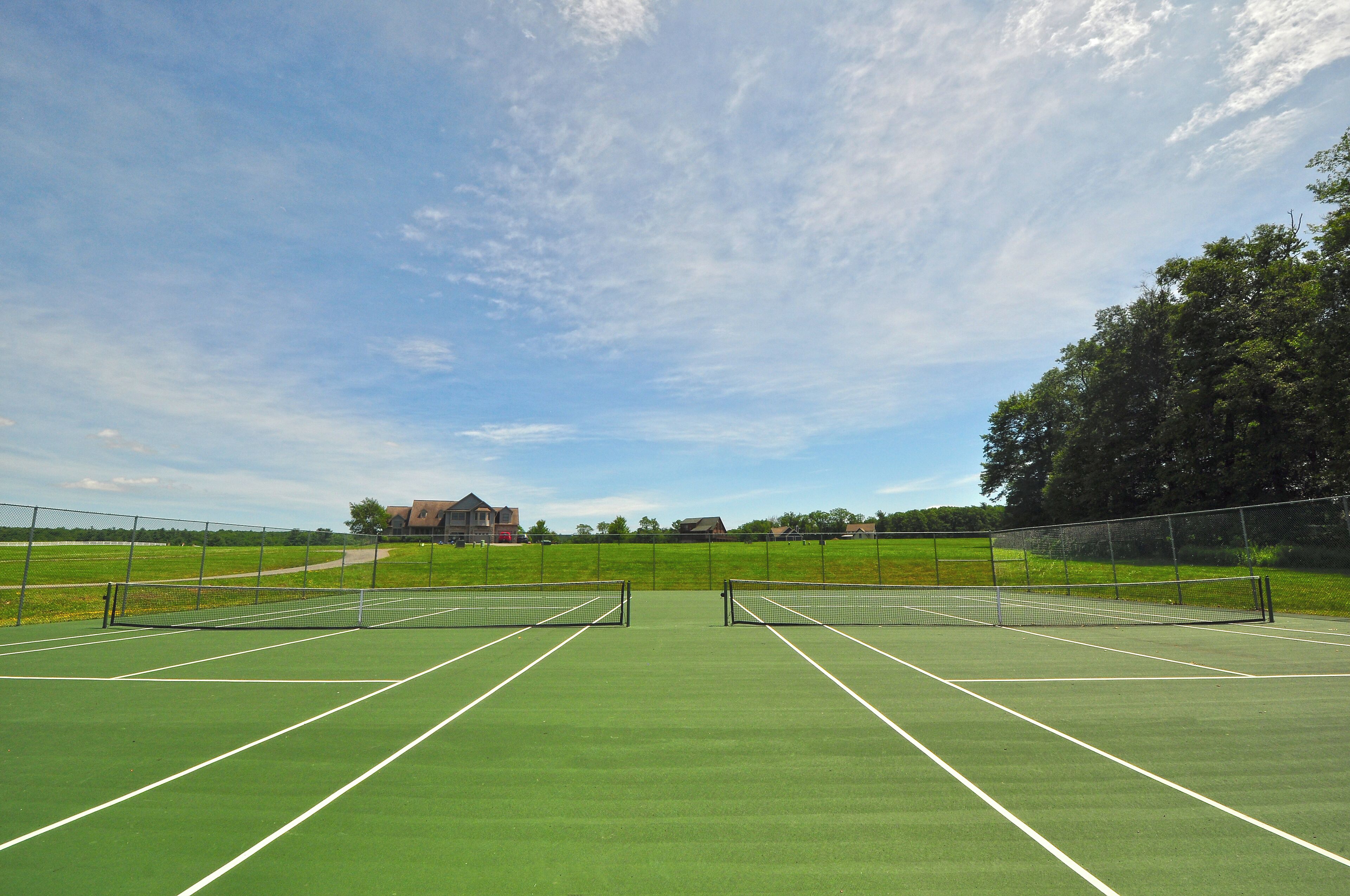 A tennis court with a net, surrounded by a fence, and houses in the background.