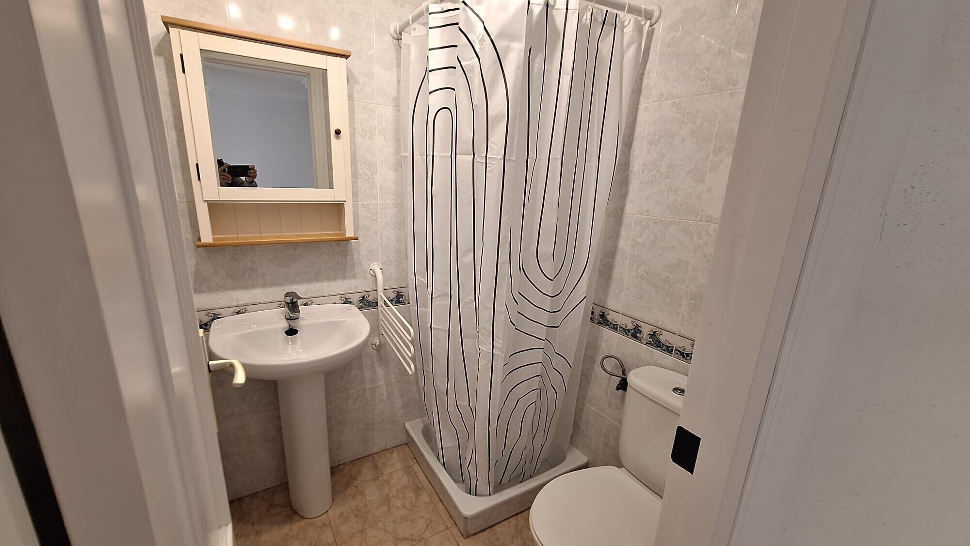 A bathroom with a sink, mirror, toilet, and shower curtain.