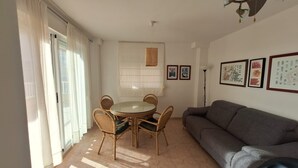 En stue med et rundt glasbord, fletstole, en grå sofa og en loftsvifte.