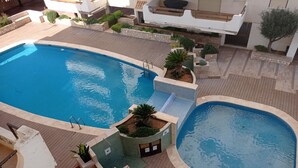 A large outdoor swimming pool with a wooden deck surrounding it, a smaller adjacent pool, and a seating area with plants.