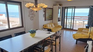 A dining area with a table and chairs, a yellow sofa, and a view of the beach through large windows.