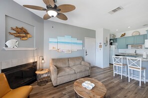 A modern living room with a fireplace, a sofa, a coffee table, and a ceiling fan. - Relaxing Beach Escape With Balcony, Pool Access, and Short Walk to Shore (Corpus Christi)