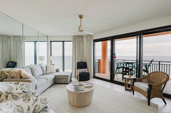 A modern living room with a sofa, armchairs, a coffee table, and a balcony with outdoor furniture.