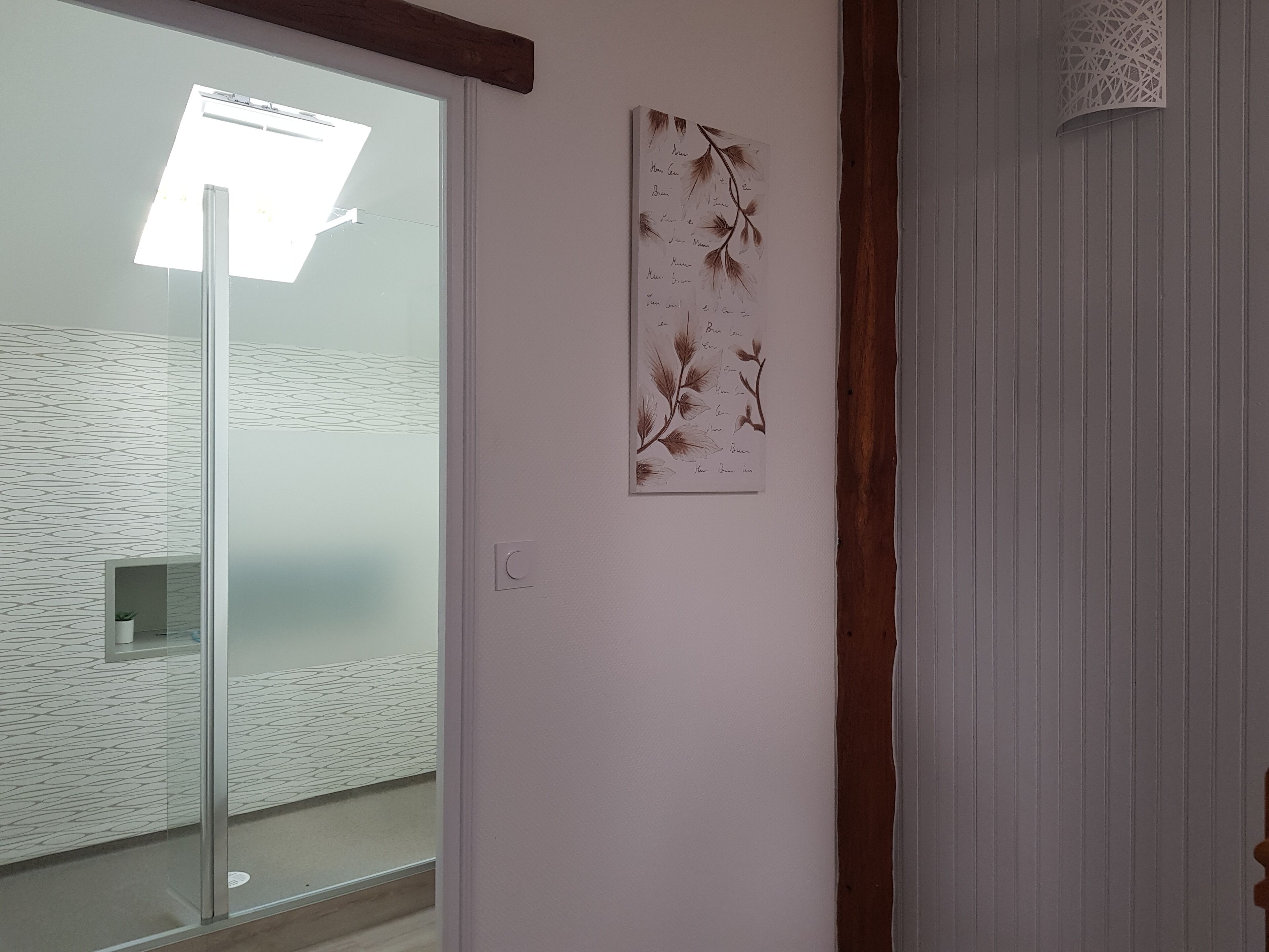 Una habitación con puerta de cristal, una obra de arte en la pared con ramas y una viga de techo de madera.