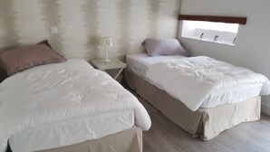 A bedroom with two beds, a nightstand, a window with a view, and a wall-mounted shelf. - In the countryside for Prof et Voyageur (Moncontour)