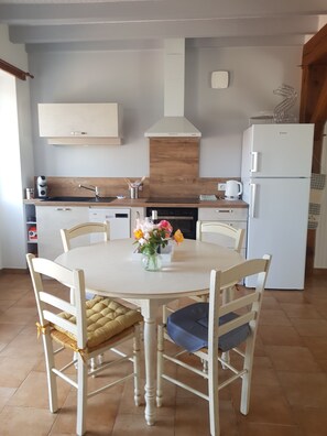 A kitchen with a round dining table, chairs, a refrigerator, and a stove.
