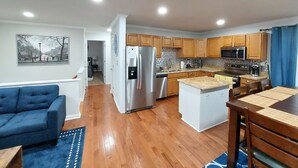 A modern kitchen with wooden cabinets, stainless steel appliances, and a dining area with a blue sofa and a wooden table.