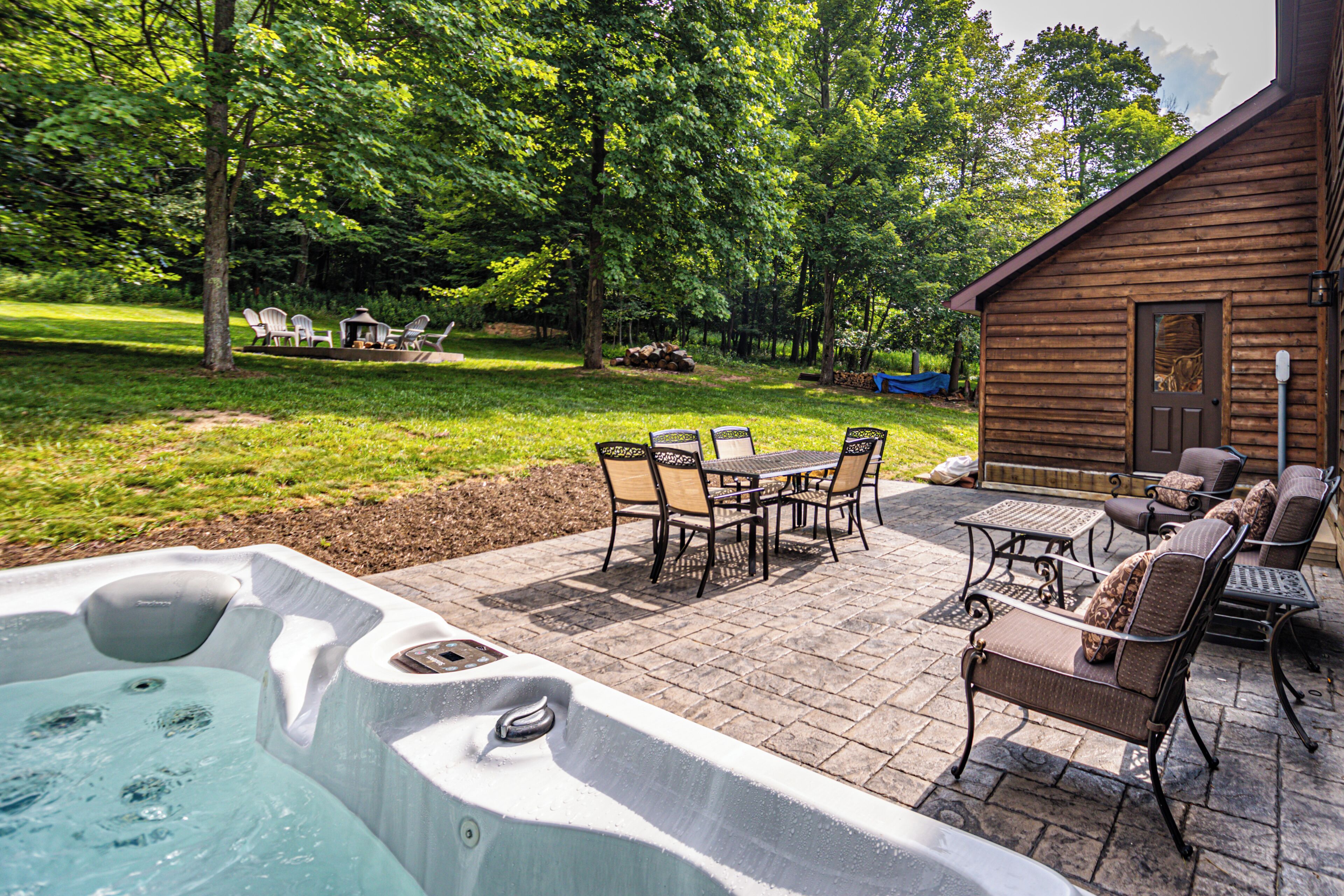 A hot tub, patio furniture, and a wooden cabin in a lush backyard.