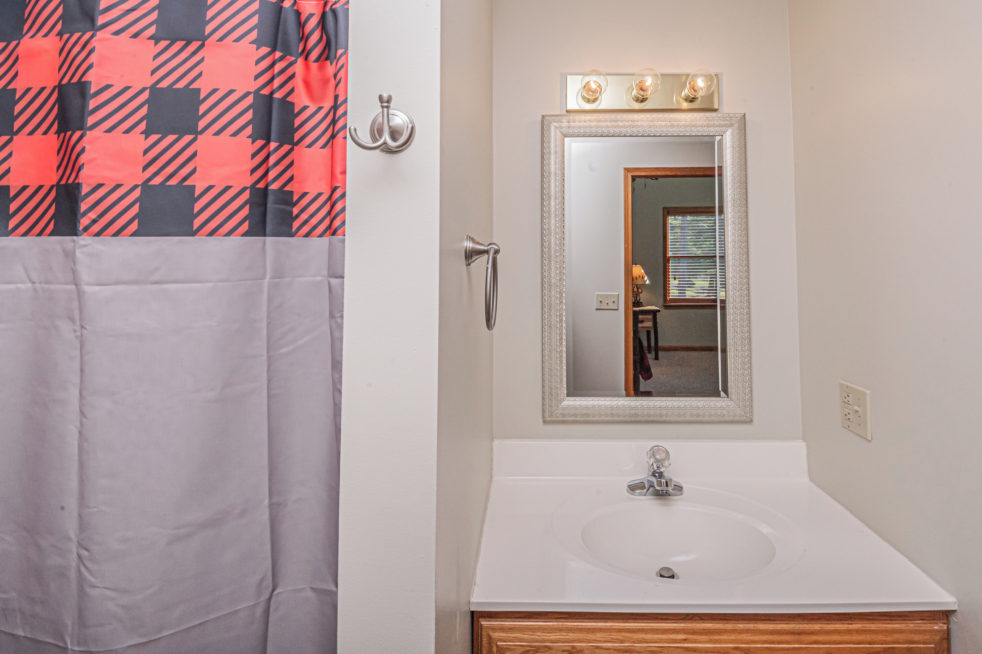 A bathroom with a white sink, a mirror with lights, and a towel rack.