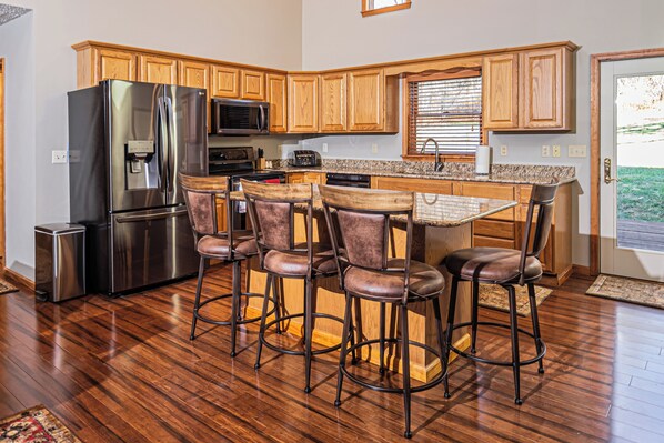 A kitchen with wooden cabinets, a stainless steel refrigerator, a microwave, a sink, and a bar area with stools. - Dancing Bear Lodge by Taylor Made Deep Creek (McHenry)