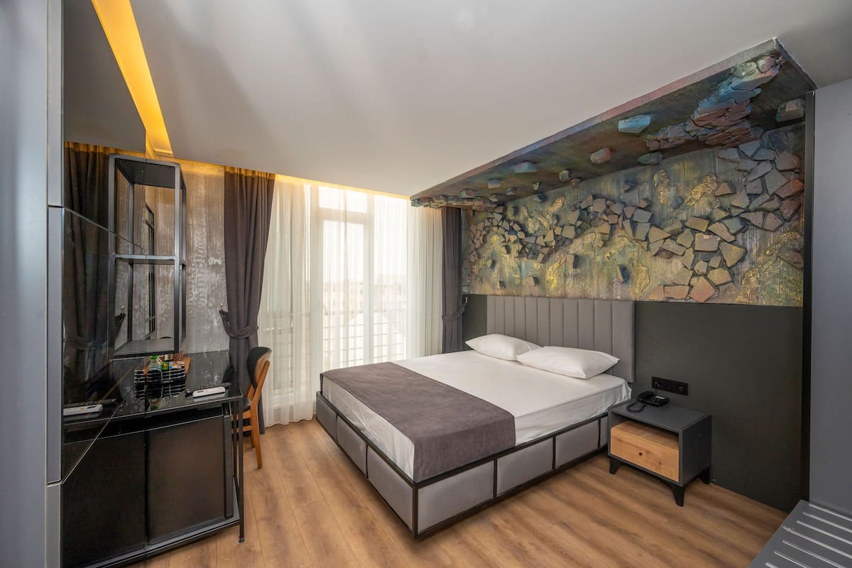 Una habitación de hotel moderna con cama, mesita de noche, escritorio con silla y un gran mural de piedra.