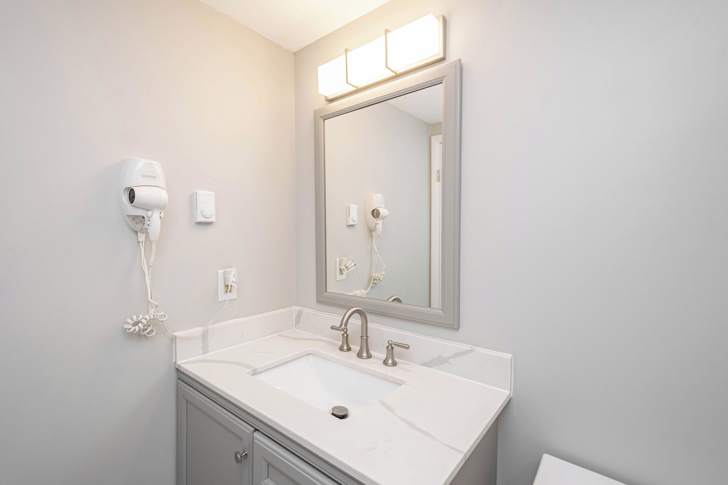 A bathroom with a white sink, a large mirror, and a hairdryer mounted on the wall.