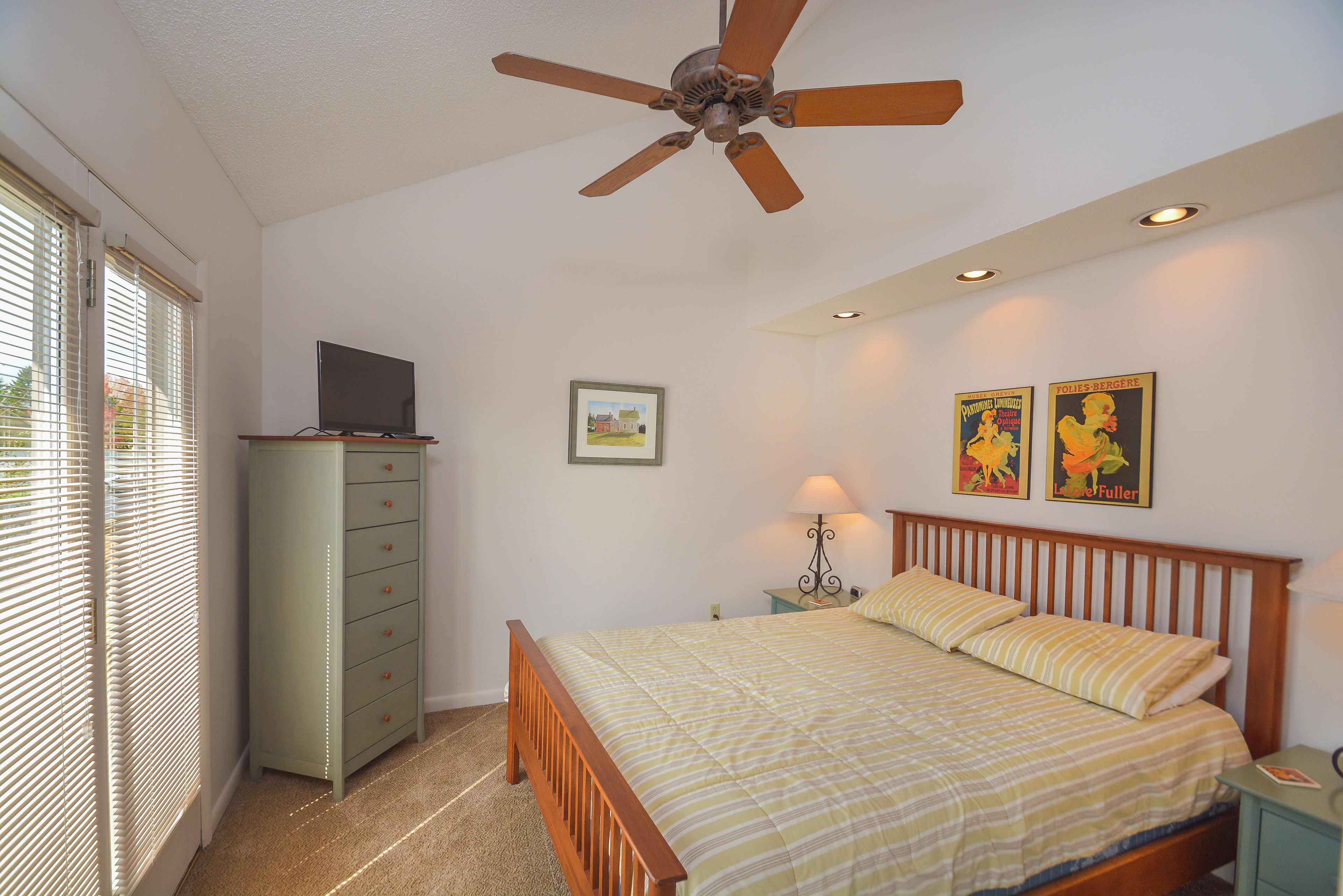 Quarto com cama, penteadeira, ventilador de teto e duas luminárias de parede.