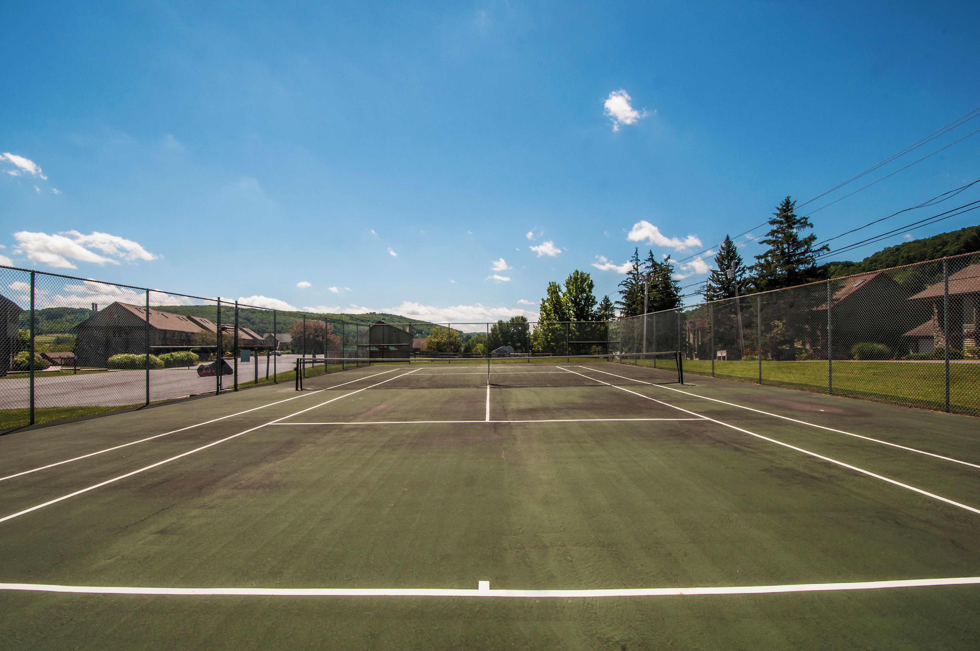 An outdoor tennis court with a net in the center, surrounded by a fence.