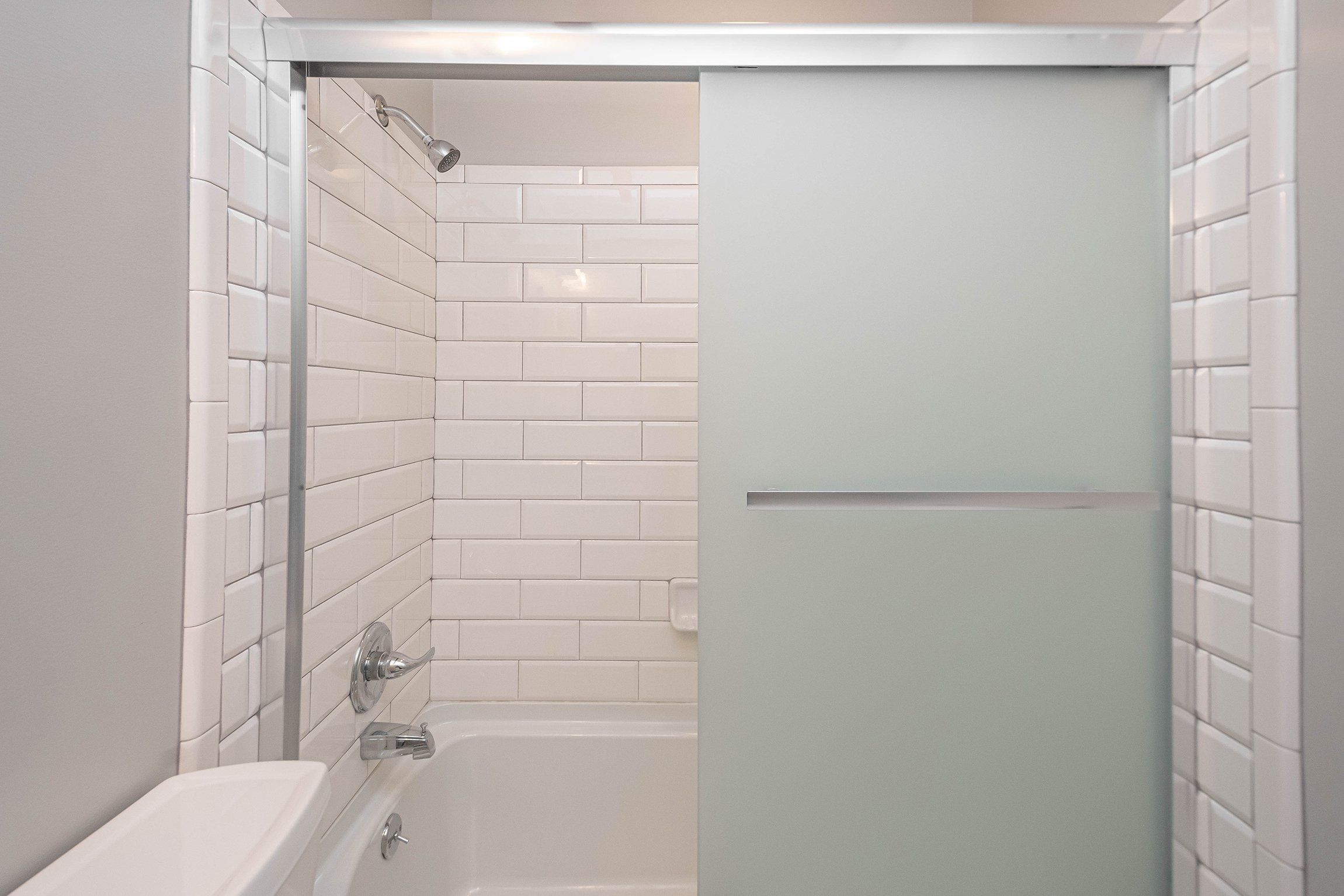 A bathroom with white tiled walls, a bathtub, and a shower enclosure.