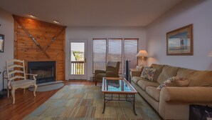 Ein gemütliches Wohnzimmer mit Kamin, Holzwänden, einer Couch, einem Couchtisch und einem Sessel.